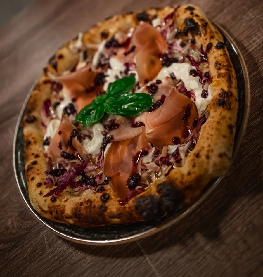 La pizza Mirtilla sul tavolo di legno: radicchio, speck, stracciata, mirtilli e una foglia di basilico al centro