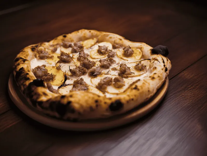 Pizza bianca con patate a fette e salsiccia sbriciolata su un piatto di legno
