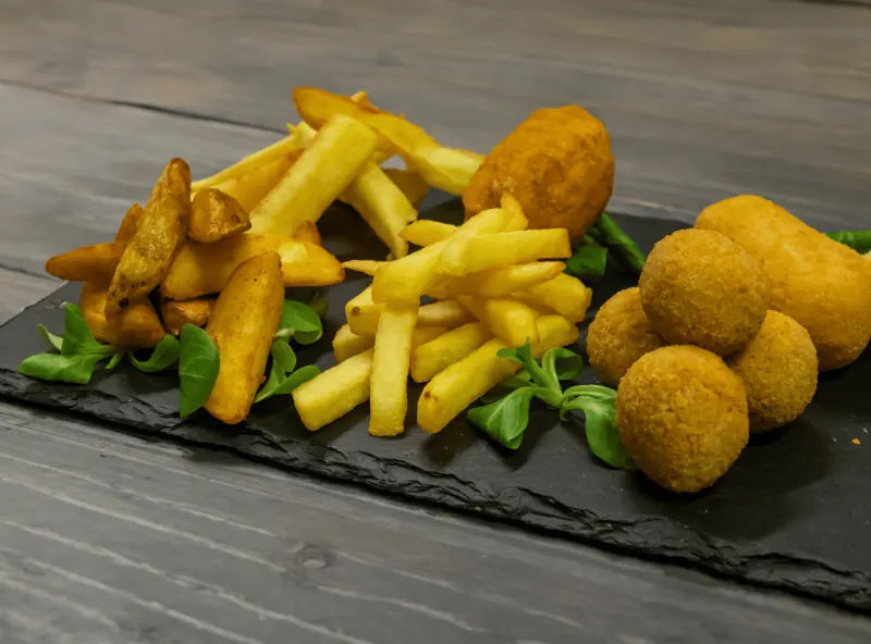 Patate a spicchi, patatine, crocchè e olive all'ascolana su una lastra di ardesia