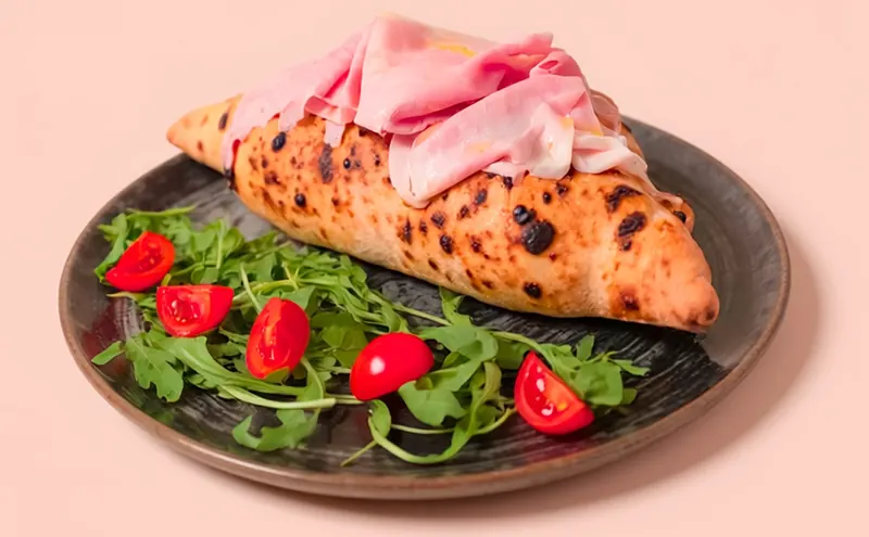Calzone con fette di prosciutto sopra, rucola e pomodorini nel piatto