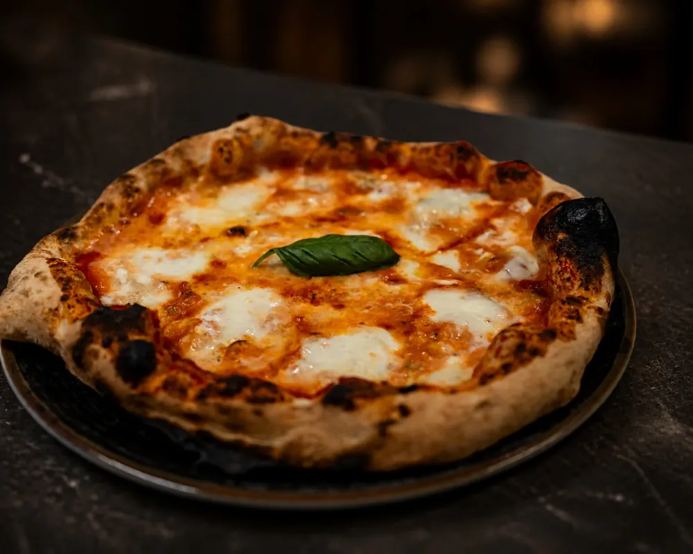 Margherita con una foglia di basilico al centro, su un piatto scuro